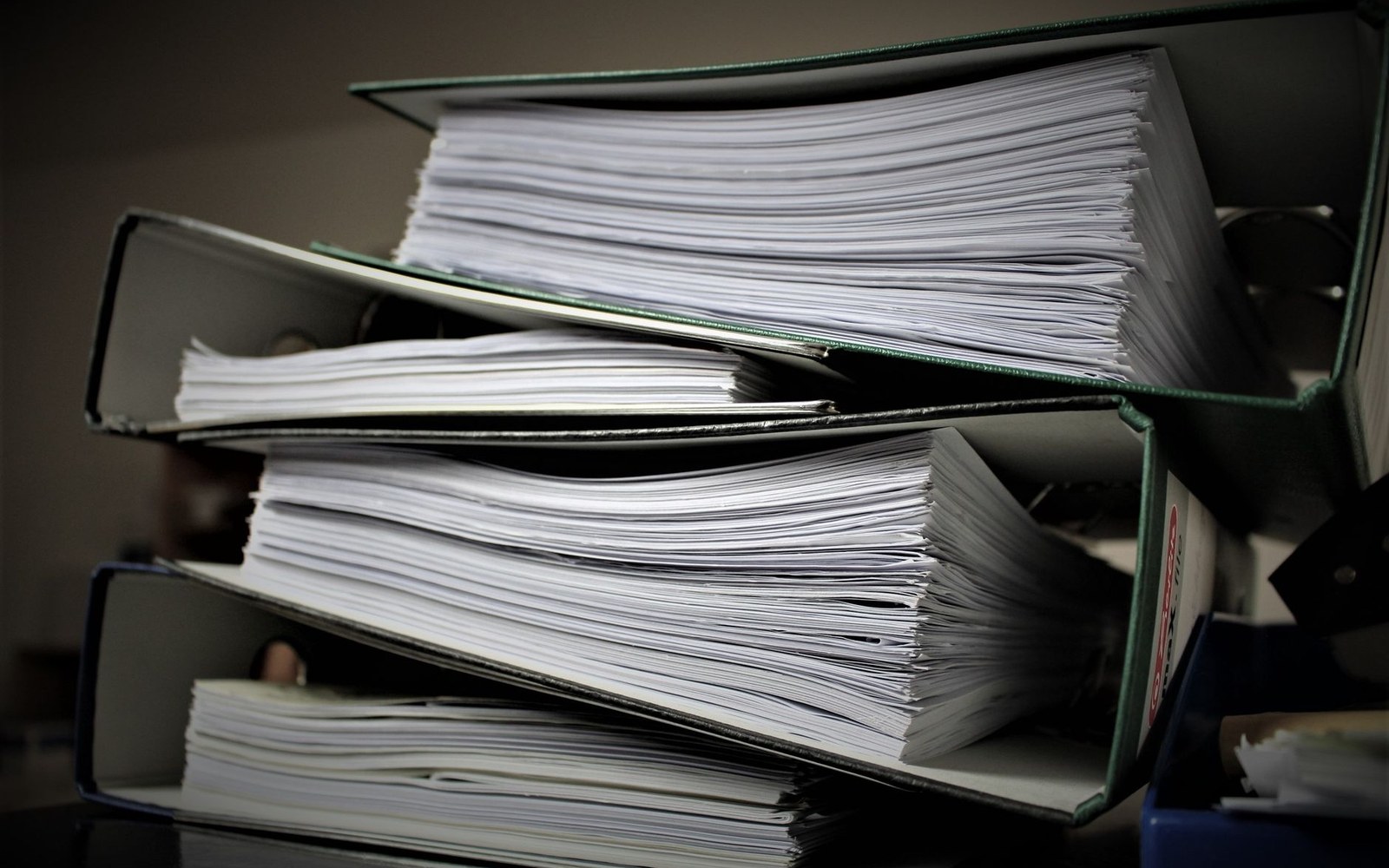 Stack of thick paper-filled binders piled on top of each other on a desk
