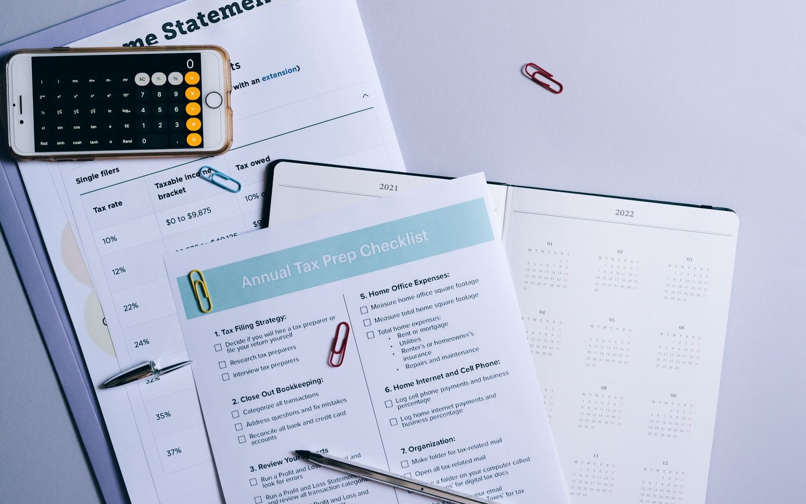 Tax prep checklist and income tax rate table next to a calculator app and calendars