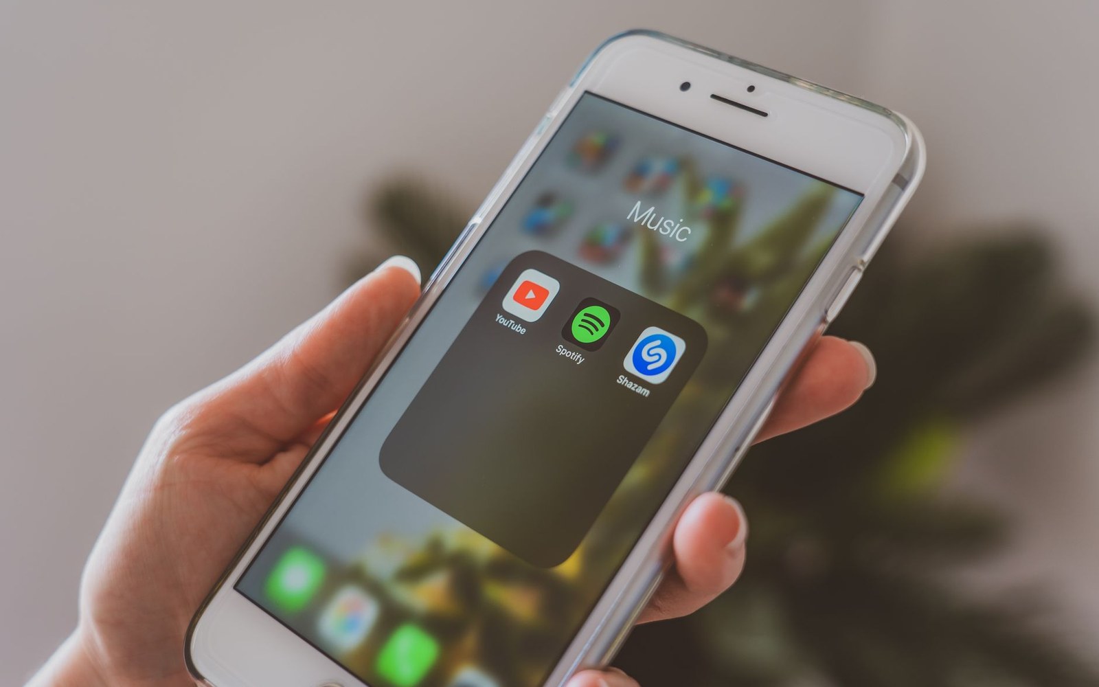Hand holding a smartphone showing a music folder with YouTube, Spotify and Shazam icons