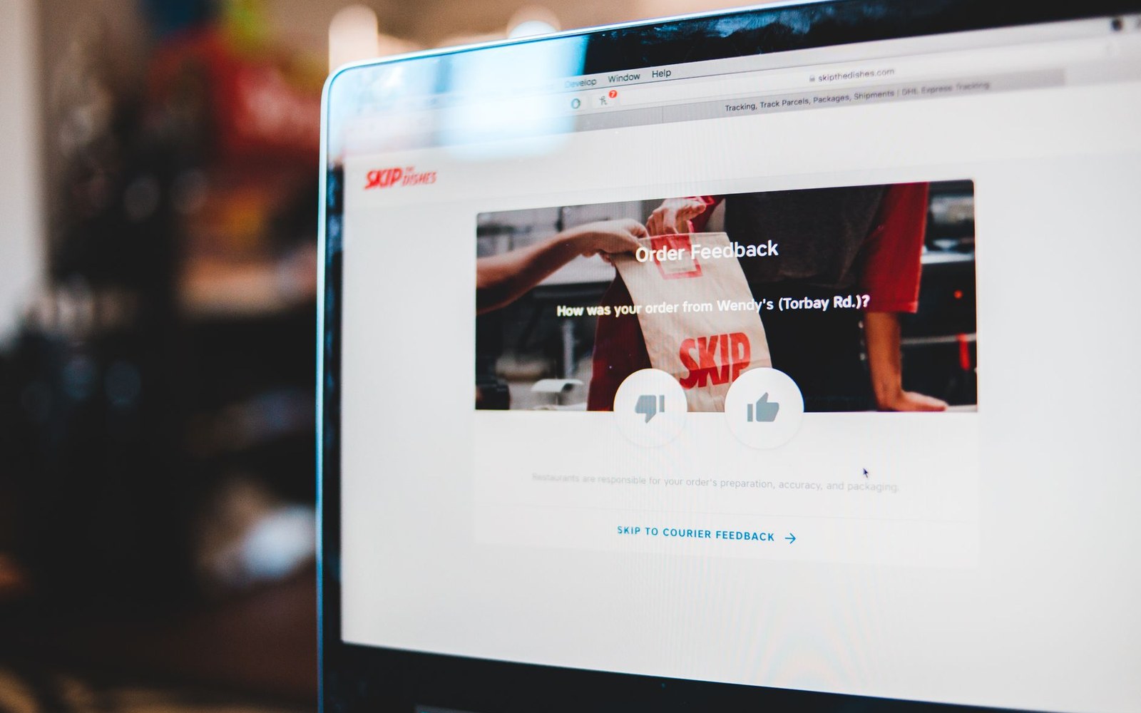 Laptop screen showing a Skip the Dishes order feedback page with thumbs up and down icons