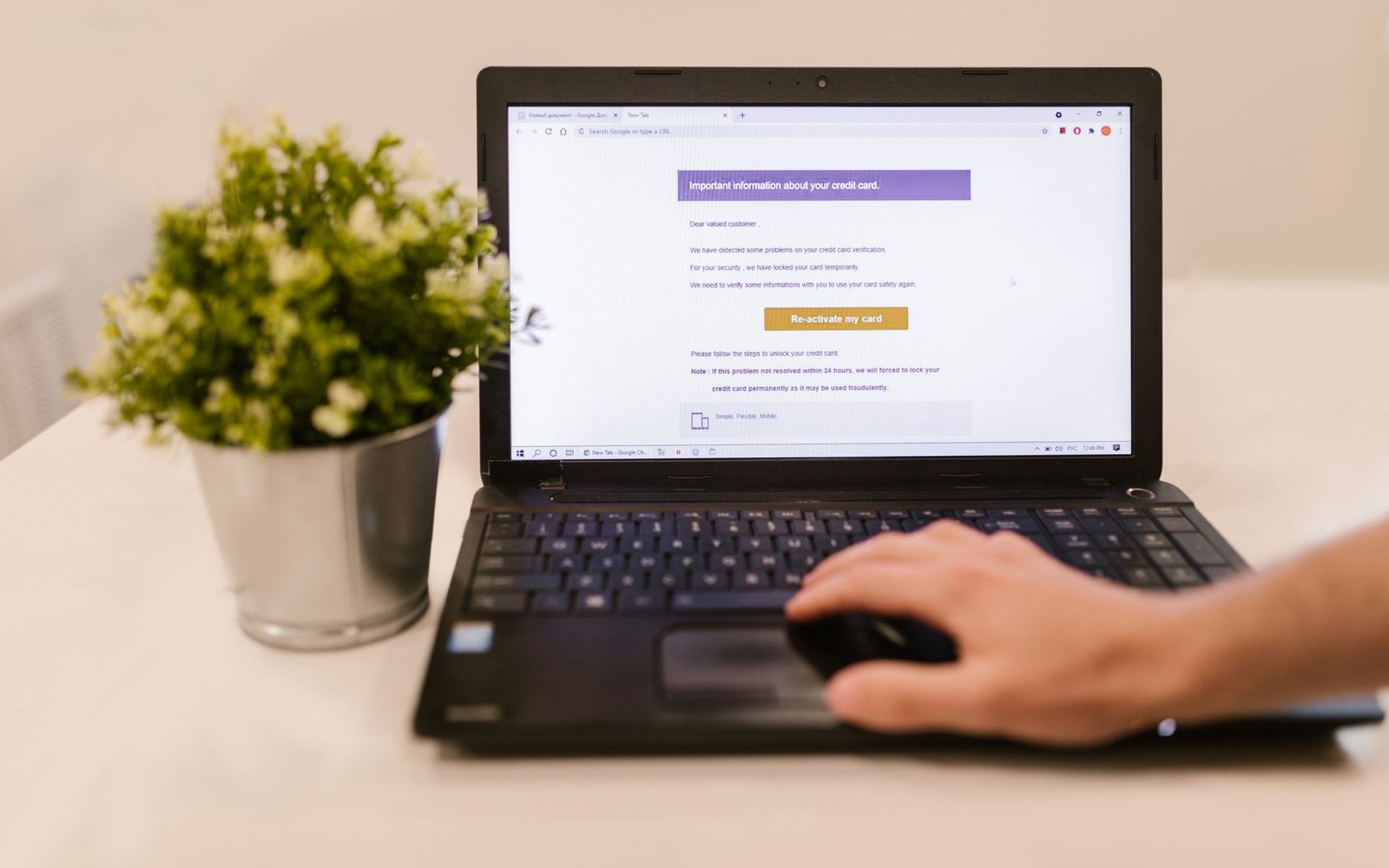 A hand uses a laptop mouse beside a screen showing a suspicious credit card verification message
