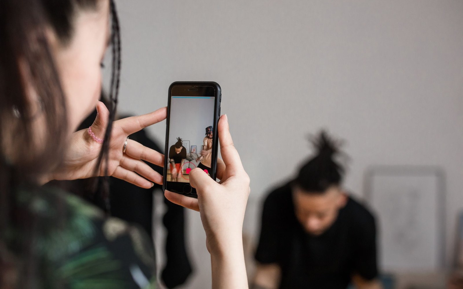 Woman holds up a smartphone to photograph a seated man with dreadlocks