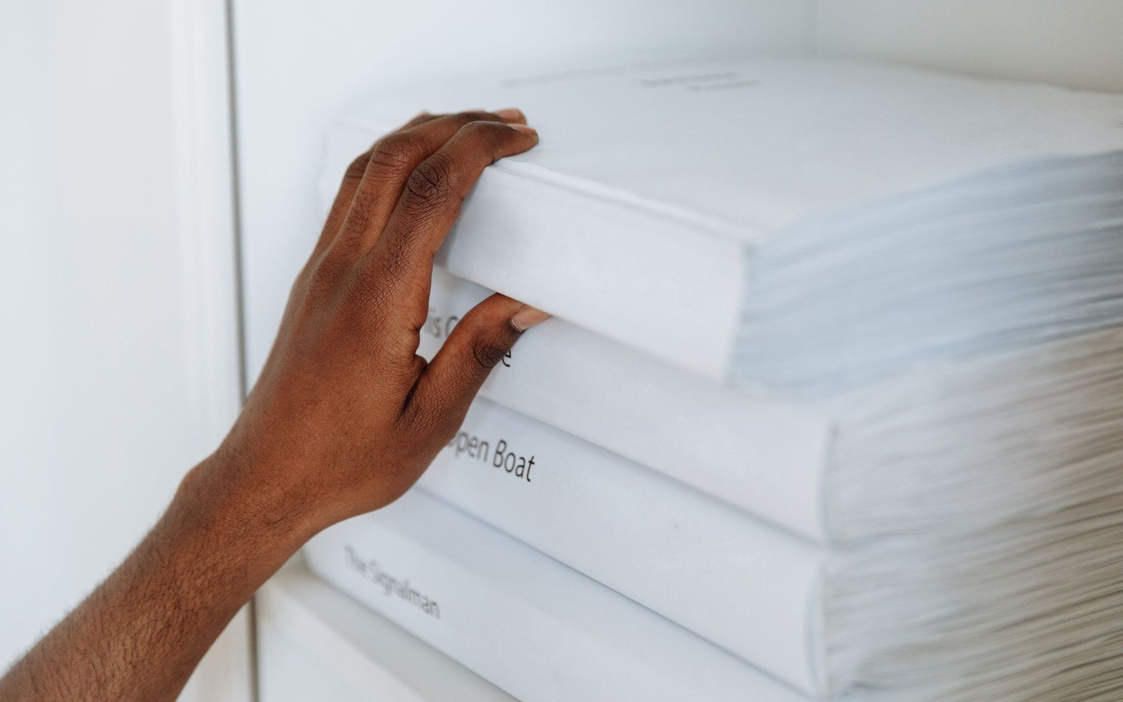 A hand pulls a white book from a stacked shelf of plain white volumes